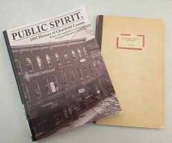 Two books laying on a flat surface. The cover of one item show a brick building.